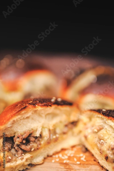 Fototapeta Homemade beef burger with cheese sliced in half with other burgers on the side on a wooden board with free space for text/decoration. Interior view of the burger.