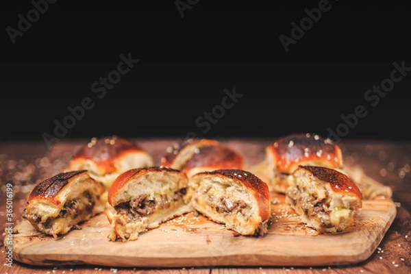 Fototapeta Homemade beef burger with cheese sliced in half with other burgers on the side on a wooden board with free space for text/decoration. Interior view of the burger.
