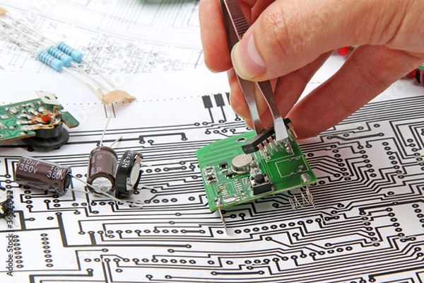 Fototapeta A hand hand with tweezers holding a electronic circuit board on