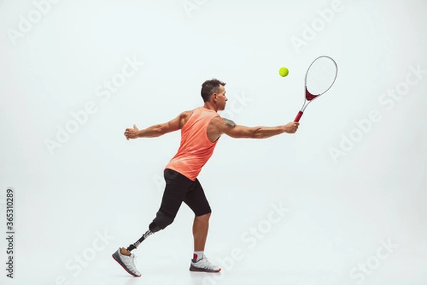 Fototapeta Athlete with disabilities or amputee isolated on white studio background. Professional male tennis player with leg prosthesis training in studio. Disabled sport and healthy lifestyle concept.