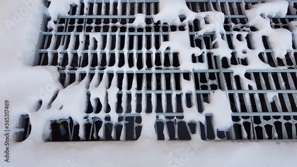 Fototapeta Close-up of white pieces of snow on a metal grate. Snow falls through the grating, revealing voids. Abstraction of snow and metal lattice. On a winter day, outdoors in the evening. Texture.