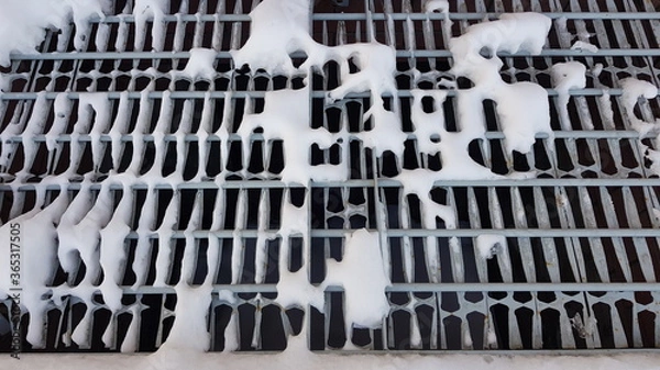 Fototapeta Close-up of white pieces of snow on a metal grate. Snow falls through the grating, revealing voids. Abstraction of snow and metal lattice. On a winter day, outdoors in the evening. Texture.