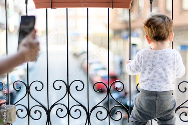 Obraz A year and a half old boy playing on the balcony and watching the cars go by in the quarantine