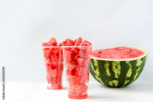 Fototapeta sliced pieces of ripe, juicy, sweet watermelon inside a long, plastic Cup on a light background front view. The concept of light, summer food.