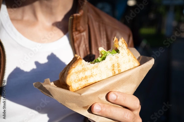 Fototapeta Fast food sandwich toast  in the hands of a guy, bitten off. Snack on the street