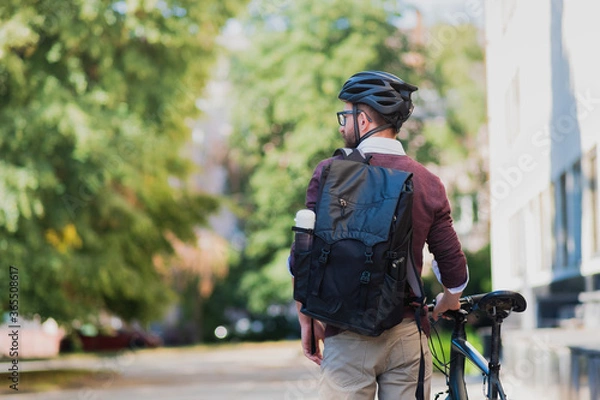 Fototapeta Male commuter or messenger with a bike in urban background. Safe cycling in the city, going to work by bicycle, delivery man image