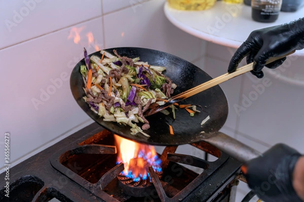Obraz Chef making japonese food. Stir-fry soba noodles with beef and vegetables in wok pan on dark background
