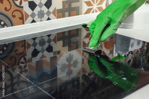 Obraz Human hand in a glove cleaning a ceramic hob with a scraper