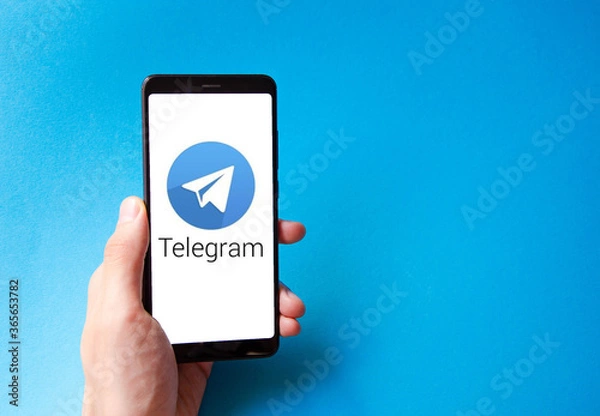 Fototapeta A male hand holds a smartphone, points a finger, types. Communication on a smartphone, correspondence. Place for text. Smartphone in hand on a blue  background.