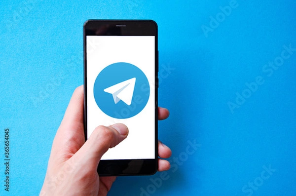 Fototapeta A male hand holds a smartphone, points a finger, types. Communication on a smartphone, correspondence. Place for text. Smartphone in hand on a blue  background.