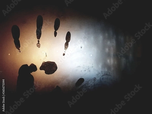 Fototapeta Abstraction, handprint on cold or misted glass, in the dark. Mysterious fingerprint with the effect of mystery and mysticism. Cover for a detective story or unsolved mystery. Palm on glass.