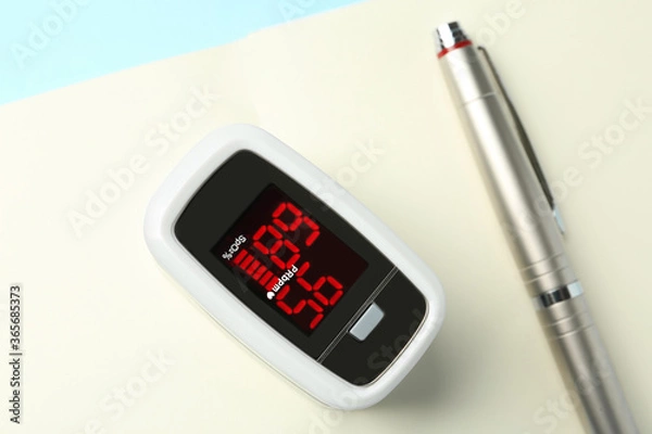 Fototapeta Modern fingertip pulse oximeter, pen and open notebook on light blue background, flat lay