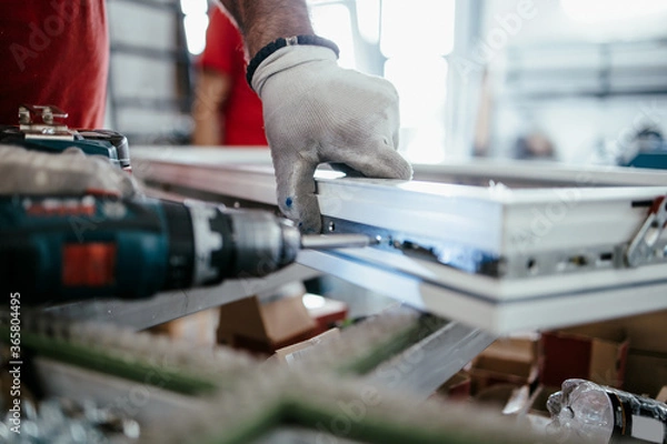 Fototapeta Manual worker assembling PVC doors and windows. Manufacturing jobs. Selective focus. Factory for aluminum and PVC windows and doors production.