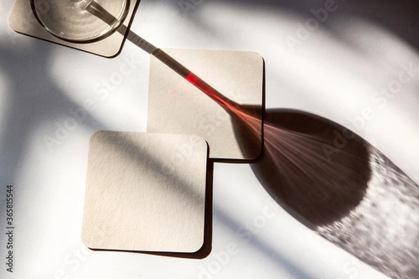 Fototapeta shadow of a glass of red wine with coasters under the sun