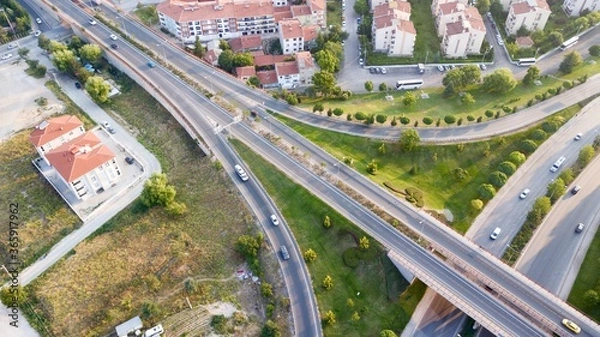 Fototapeta Aerial view of the roundabout on the river. Trees, overpass, buildings and vehicles can be seen. 