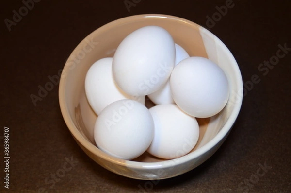 Fototapeta white chicken eggs in a two-color bowl located on a dark background