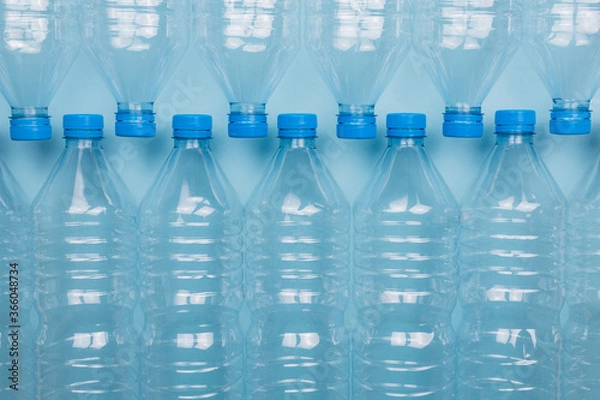 Fototapeta Empty clear plastic bottles with caps stacked on a blue background. Recycling and environment concept.