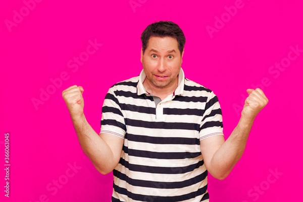 Fototapeta Joyful man in striped t-shirt gesturing index finger hand on camera isolated over magenta background