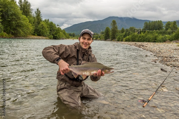 Fototapeta A fisherman holding up a male humpback pink salmon while wading in a river.