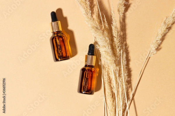 Fototapeta Natural cosmetics in glass bottles with dropper on a beige background with bright sunlight. Natural cosmetics concept, natural essential oil