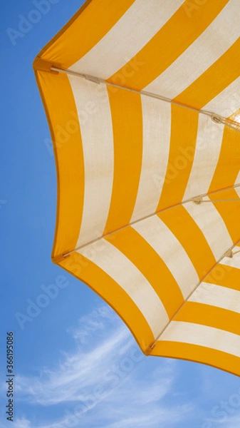 Fototapeta White and yellow striped beach umbrella. Blue sky in the background. View from below. Relaxing context. Summer holidays by the sea. General contest and location
