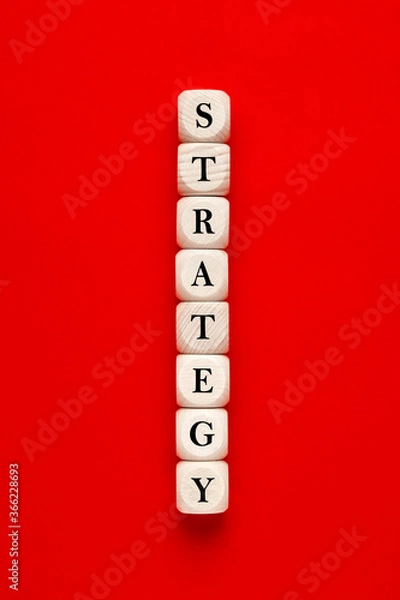 Fototapeta The word strategy written on wooden cubes on red background. developing or building a strategy concept.