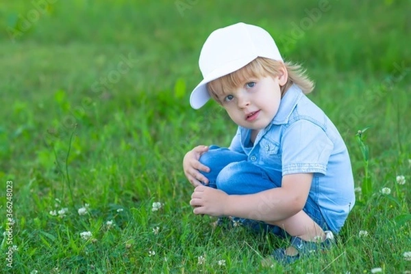 Obraz A child in a white cap sits in the Park on the grass.