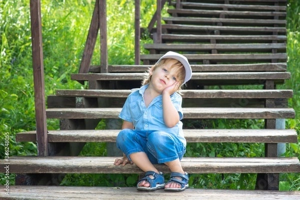 Obraz A sad boy is sitting on a wooden staircase in the Park and is bored.