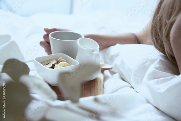 Fototapeta 爽やかな朝に寝室のベッドでくつろぐ白いワンピースの女性