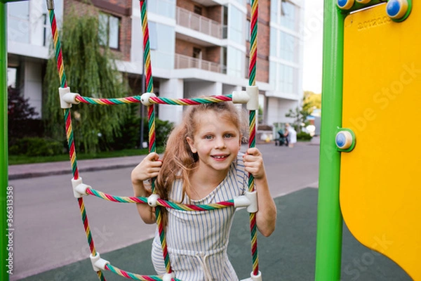Fototapeta Portrait of girl climbing at the playing rope at the playground.