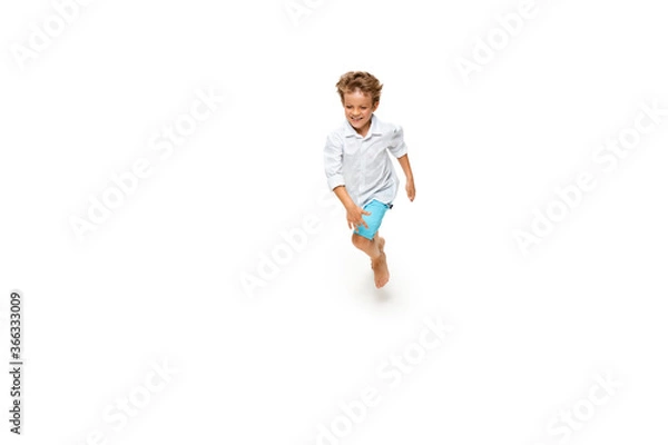 Fototapeta Happy child, little and emotional caucasian boy jumping and running isolated on white background. Looks happy, cheerful, sincere. Copyspace for ad. Childhood, education, happiness concept.