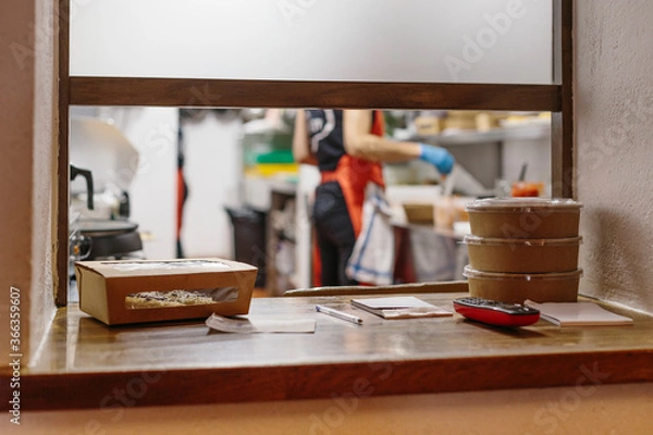 Fototapeta Cooks in a restaurant preparing takeaway food. The containers used are compostable.