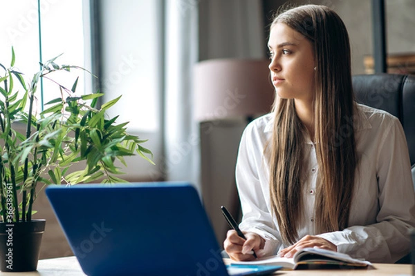 Fototapeta Home schooling. Beautiful caucasian female student is studying at home online using a laptop
