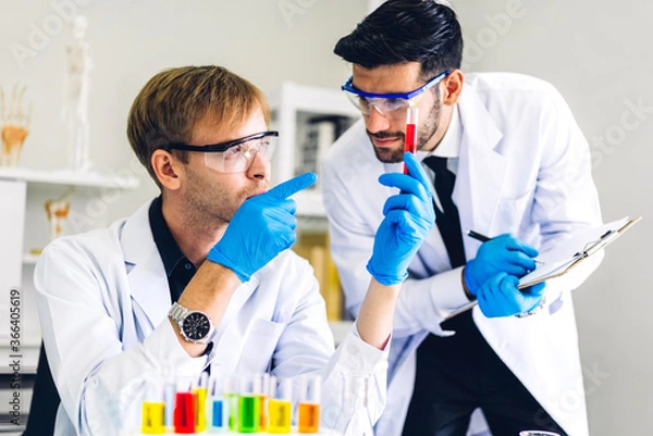 Obraz Professional two scientist man research and working doing a chemical experiment while making analyzing and mixing  liquid in test tube.Young science man dropping sample chemical on glass at laboratory