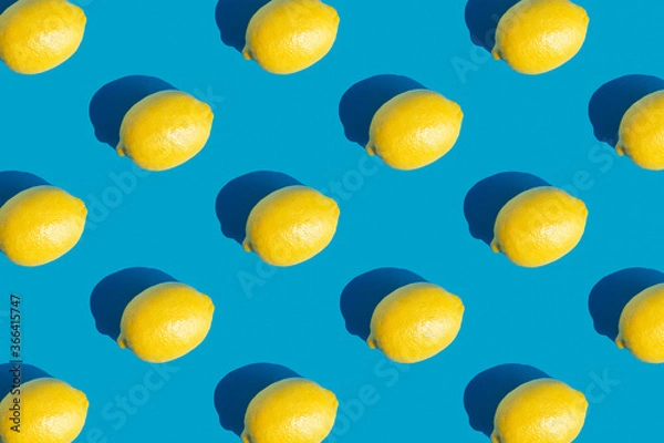 Fototapeta Pattern with ripe yellow lemon with a hard shadow on blue background. Minimum summer background. Concept of healthy eating.