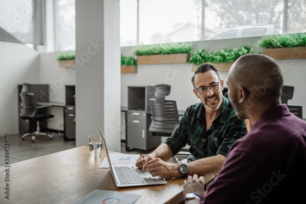 Fototapeta To diverse businessmen working on a laptop at an office table