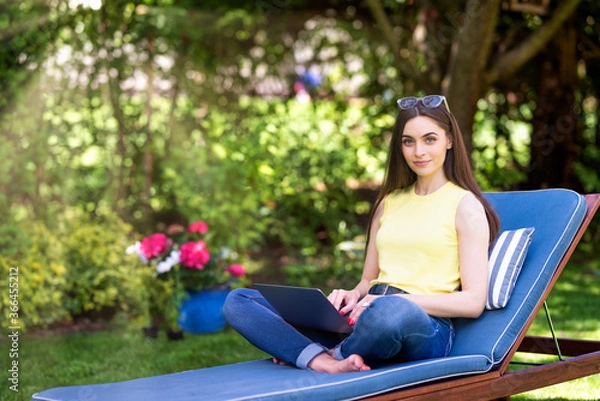 Fototapeta Young woman using laptop in the garden while working from home
