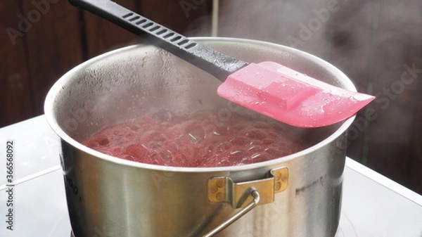 Obraz the cook cooks raspberry jam in a pot on the stove. raspberry jam.