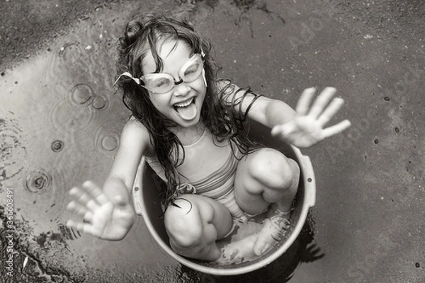 Fototapeta a girl in swimming glasses splashes water while sitting in a basin on the street. black-white