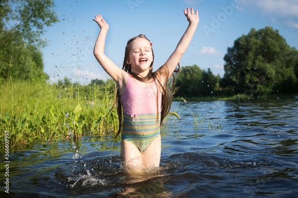 Fototapeta a little girl in a bathing suit jumps and splashes water in the lake in summer
