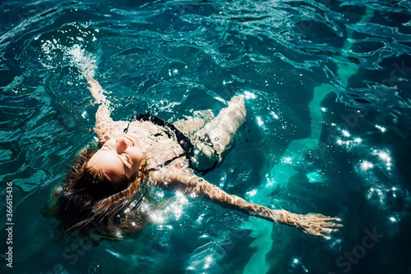 Fototapeta Young hot woman resting alone. Girl swimming in water and enjoying. Rest and relax under the sun outside. Resort spa place and joy because of swimming. Spa procedure.