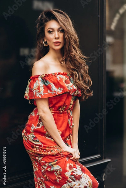 Fototapeta Girl in red dress stands on a street. Soft selective focus