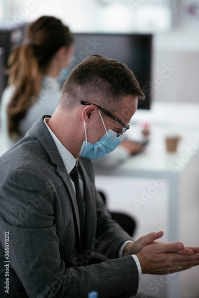 Obraz Close up of businessman disinfecting hands in the office.	