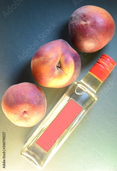 Fototapeta three ripe peaches close-up over a bottle with a pink label on an embossed leathery azure green background, top view