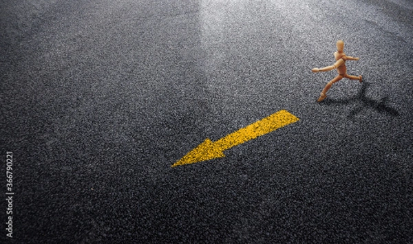 Fototapeta Abstract image of Wooden model running follow yellow arrow traffic signs on asphalt road.