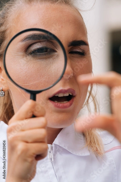 Obraz A female doctor in a white robe looks through a magnifying glas