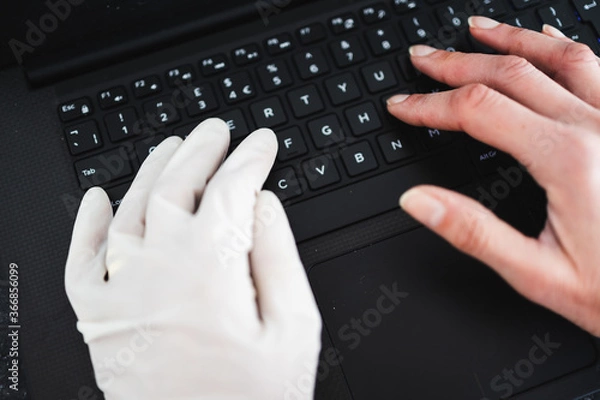 Fototapeta hand typing on shared computer keyboard at work wearing disposable glove to avoid contact with potentially infected surfaces and other hand without glove