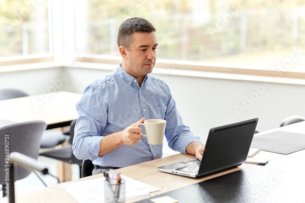 Fototapeta remote job, business and people concept - middle-aged man with laptop computer working at home office and drinking coffee