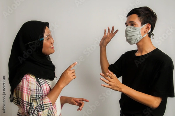 Fototapeta Young Asian teen wearing non-medical mask or face shield and do social distancing as health protocol in new normal era for preventing corona virus / covid-19 while interacting