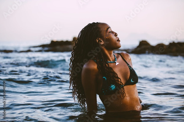 Fototapeta An elegant and beautiful young black woman in bikini in a beach in the sunset time  in summer. 